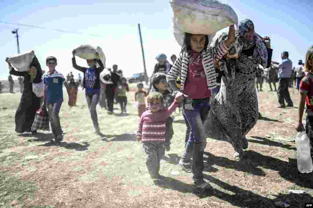 Syrian Kurds carry their belongings after they crossed the border between Syria and Turkey near the southeastern town of Suruc, Sanliurfa province, Turkey, Sept. 20, 2014. 