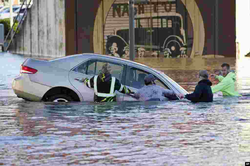 People try to stop the car from floating further into the flooded Nooksack River in Ferndale, Washington, Nov. 16, 2021.