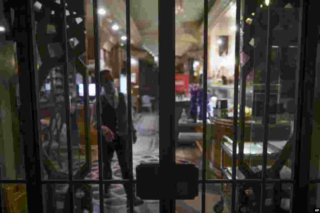 A staffer stands behind the bars of a closed restaurant, in Rome, Monday, Oct. 26, 2020. For at least the next month, people outdoors except for small children must now wear masks in all of Italy, gyms, cinemas and movie theaters will be closed, ski slope