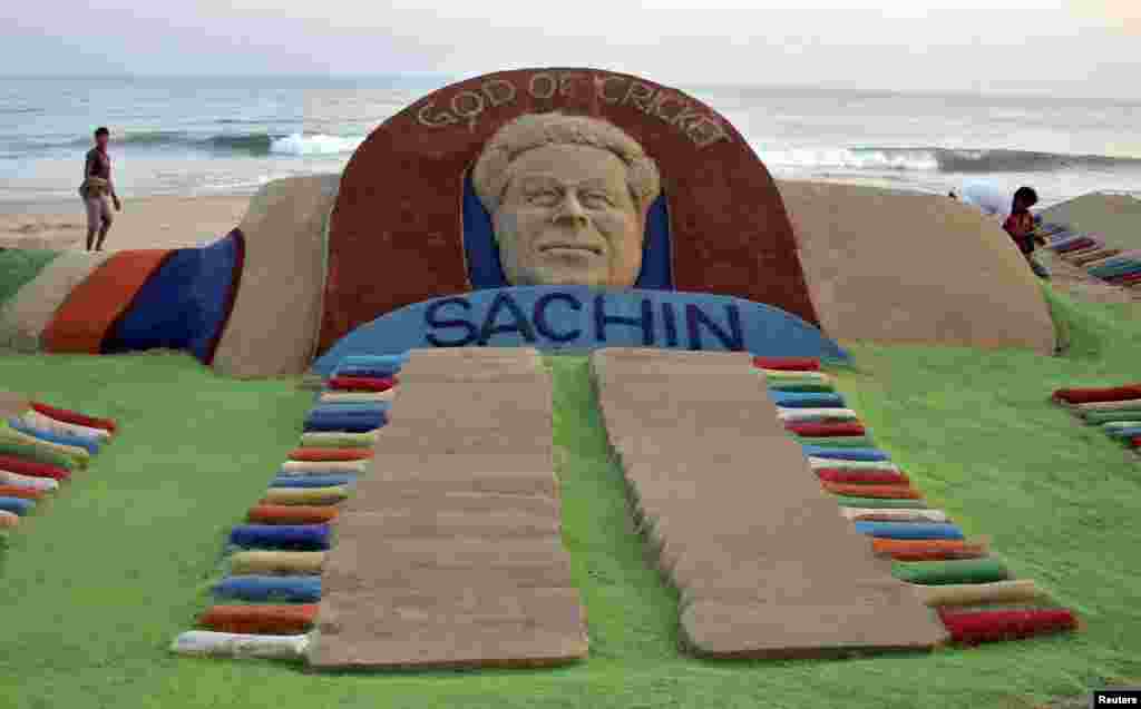 People walk past a sand sculpture of cricketer Sachin Tendulkar created by Indian sand artist Sudarshan Patnaik, in the eastern Indian state of Odisha, Nov. 13, 2013.