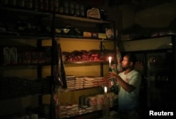 FILE - Mulugeta Desalegn, an owner of a convenience store, picks an item for a customer as he holds a candle, in Senaone, Soweto, South Africa, March 18, 2019.