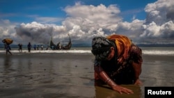 An exhausted Rohingya refugee woman touches the shore after crossing the Bangladesh-Myanmar border by boat through the Bay of Bengal, in Shah Porir Dwip, Bangladesh, Sept. 11, 2017.