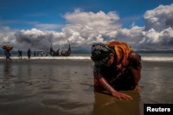 FILE - An exhausted Rohingya refugee woman touches the shore after crossing the Bangladesh-Myanmar border by boat through the Bay of Bengal, in Shah Porir Dwip, Bangladesh, Sept. 11, 2017.