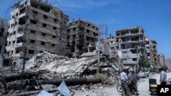 FILE - People stand in front of damaged buildings, in the town of Douma, the site of a suspected chemical weapons attack, near Damascus, Syria, April 16, 2018. 