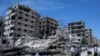 FILE - People stand in front of damaged buildings in the town of Douma, the site of a suspected chemical weapons attack, near Damascus, Syria, April 16, 2018. 