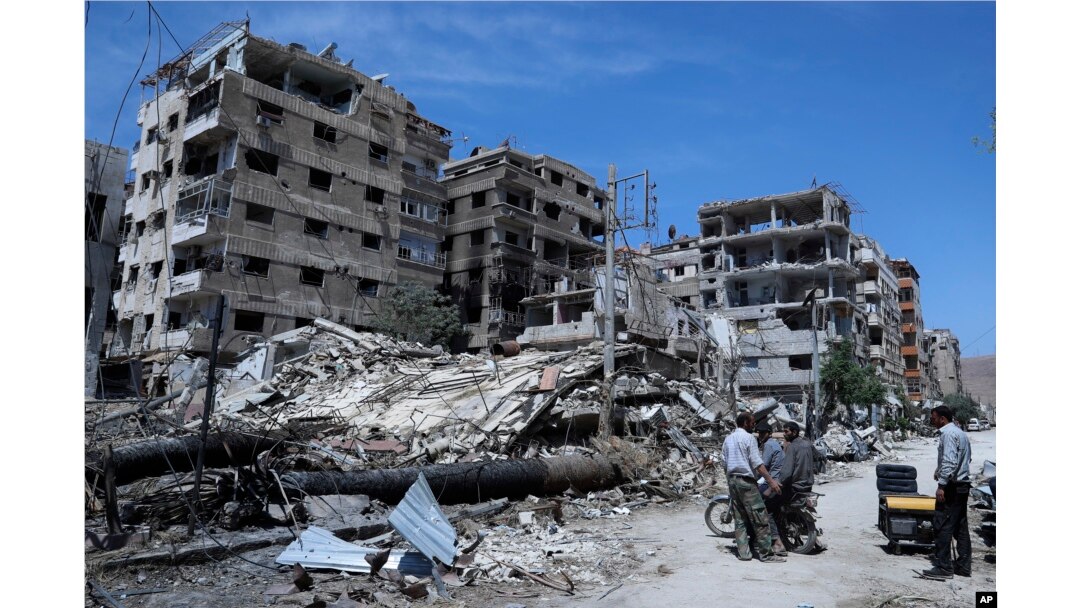 People stand in front of damaged buildings, in the town of Douma, the site of a suspected chemical weapons attack, near Damascus, Syria, April 16, 2018.