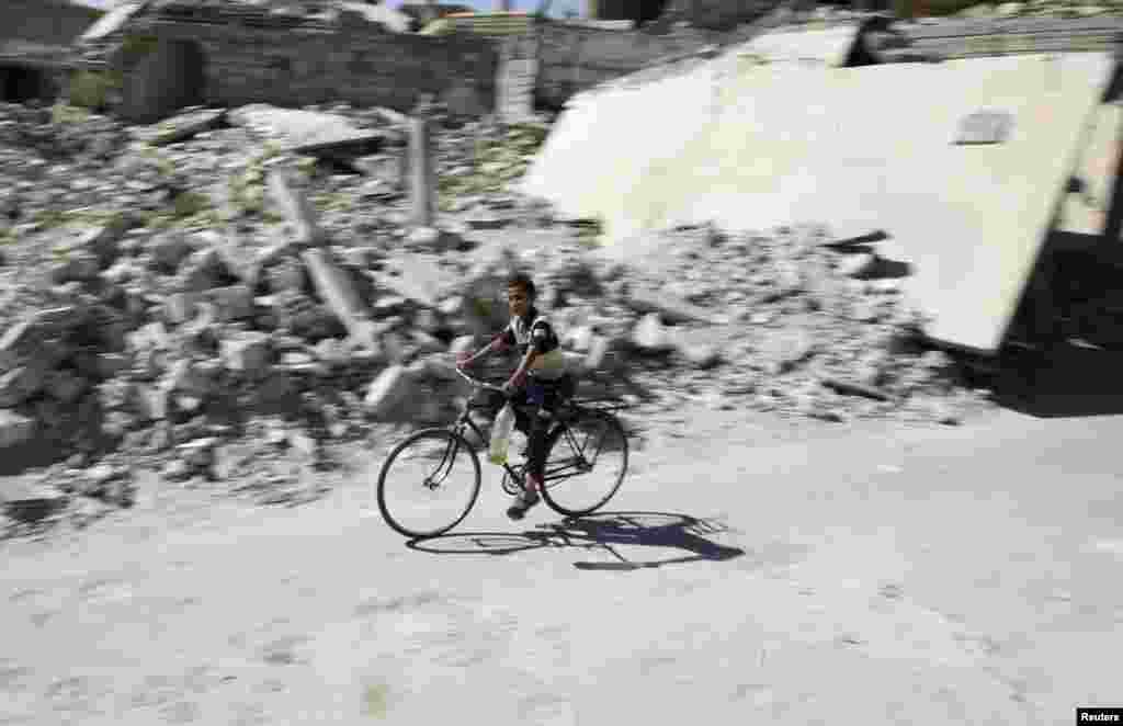 A boy rides a bicycle past damaged buildings in the rebel-held Douma neighborhood of Damascus, Sept. 25, 2016.