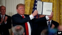 President Donald Trump shows off a "Space Policy Directive" after signing it during a meeting of the National Space Council in the East Room of the White House, June 18, 2018, in Washington. 