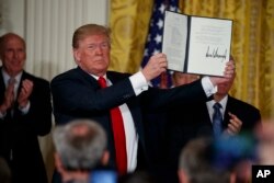 FILE - President Donald Trump hold up the "Space Policy Directive" after signing it during a meeting of the National Space Council in the East Room of the White House, June 18, 2018, in Washington.