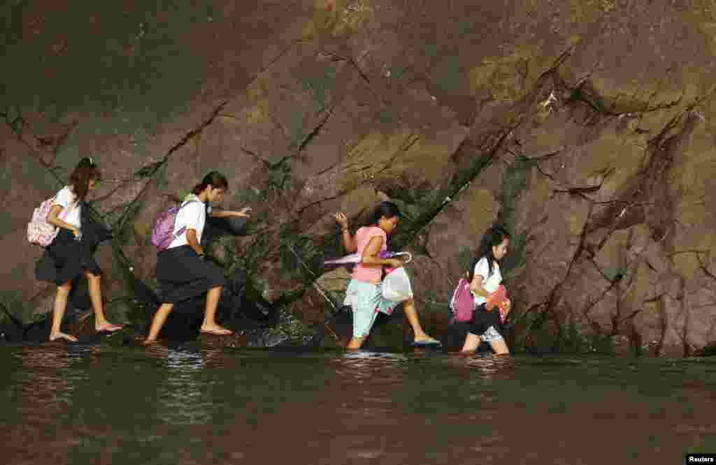 Seorang perempuan dan beberapa siswa menyusuri bagian dangkal pantai yang berbatu menuju sekolah mereka di hari pertama sekolah di Sitio Kinabuksan, desa Kawag, Subic, Zambales Province, Manila utara, Filipina.