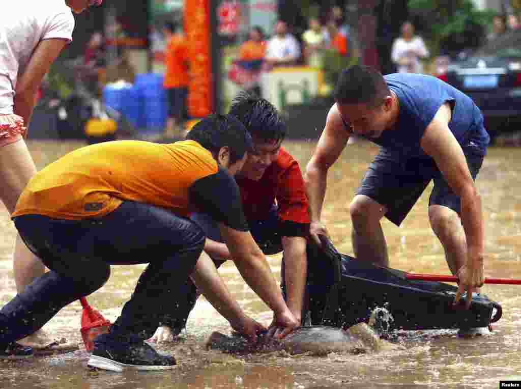 People catch a fish with a traffic cone on a flooded street after heavy rainfall in Dongguan, Guangzhou province, China, May 20, 2015.