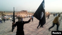 A fighter of the Islamic State of Iraq and the Levant (ISIL) holds an ISIL flag and a weapon on a street in Mosul, June 23, 2014.