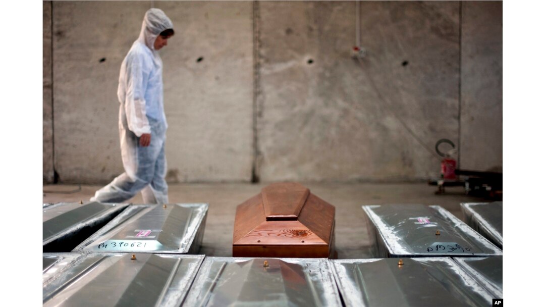 FILE - In this Oct. 8, 2016 file photo, a woman walks past rows of coffins at the NATO base in the Sicilian town of Melilli, Italy, where forensic investigator Cristina Cattaneo is one of two investigators trying to keep Italy's promise to trace the identities of all the migrants killed when an overloaded fishing boat went down off the coast of Libya on April 18, 2015.