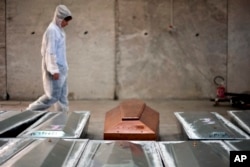 FILE - In this Oct. 8, 2016 file photo, a woman walks past rows of coffins at the NATO base in the Sicilian town of Melilli, Italy, where forensic investigator Cristina Cattaneo is one of two investigators trying to keep Italy's promise to trace the identities of all the migrants killed when an overloaded fishing boat went down off the coast of Libya on April 18, 2015.