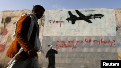 FILE - A man walks past graffiti denouncing strikes by U.S. drones in Yemen.