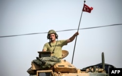 FILE - A soldier gestures as Turkish Army tanks drive to the Syrian-Turkish border town of Jarablus, Aug. 25, 2016