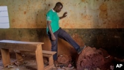 Teacher Emmy Odillo kicks at an anthill that has grown in a corner of a classroom at the now-deserted Mawero Primary School on the outskirts of Busia town, in eastern Uganda on Oct. 19, 2021. (AP Photo/Nicholas Bamulanzeki)