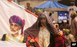 In this August 4, 2017 file photo, members of a dance troupe, in traditional garb, wait to perform next to a giant sail adorned with a portrait of the Sultan of Oman