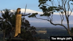 Snow on Mauna Kea is seen Friday Jan. 31, 2014, behind a statue of the Hawaiian King Kamehameha in Hilo, Hawaii.