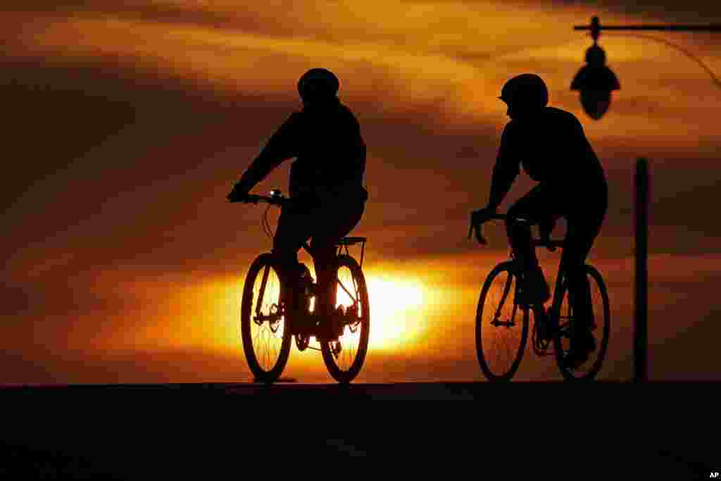 A pair of cyclists cross an empty downtown street as the sun sets, April 1, 2020, in Kansas City, Missouri.