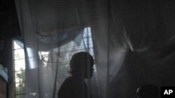 A mother and her child sit on a bed covered with a mosquito net in Africa, 30 Oct 2009