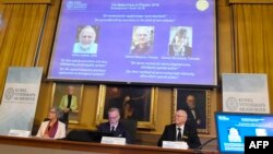 Les membres du Comité Nobel de physique Olga Botner, Goran K Hansson et Mats Larsson devant un écran présentant les portraits d'Arthur Ashkin des États-Unis, de Gérard Mourou de France et de Donna Strickland du Canada, à Stockholm, le 2 octobre 2018.