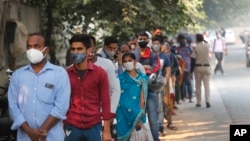 In this Nov. 6, 2020, file photo, people queue to get tested for COVID-19 as a thick quilt of smog lingers over New Delhi, India. (AP Photo/Manish Swarup, File)