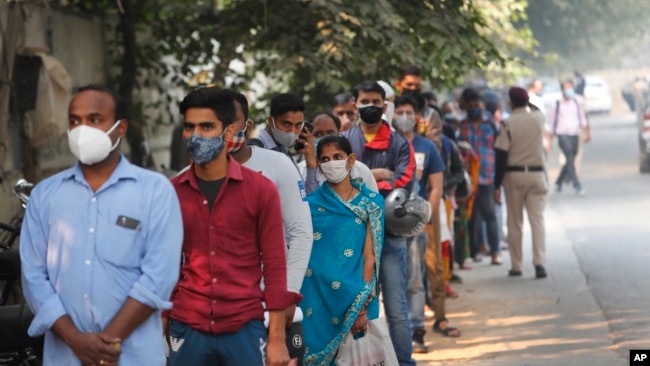 In this Nov. 6, 2020, file photo, people queue to get tested for COVID-19 as a thick quilt of smog lingers over New Delhi, India. (AP Photo/Manish Swarup, File)