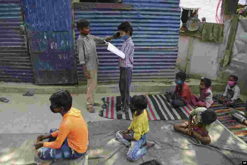 A student holds a mobile phone for another so that a fellow student can listen to instructions from a teacher as children attend online classes at a slum on the outskirts of Jammu, India.