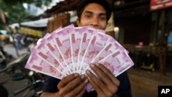 FILE - An Indian man displays new currency notes of 2000 Indian rupee in Ahmadabad, India, Nov. 11, 2016. The sudden withdrawal of 86 percent of India's currency has left cash in short supply, retail sales stumbling and wholesale markets in turmoil.