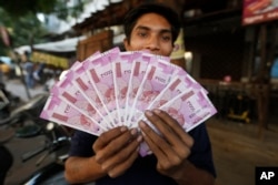 FILE - An Indian man displays new currency notes of 2000 Indian rupee in Ahmadabad, India, Nov. 11, 2016. The sudden withdrawal of 86 percent of India's currency has left cash in short supply, retail sales stumbling and wholesale markets in turmoil.