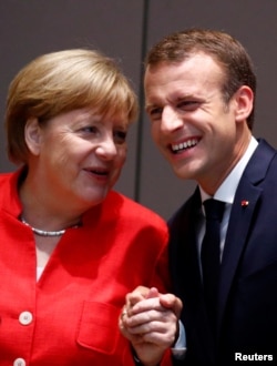FILE - German Chancellor Angela Merkel shares a laugh with French President Emmanuel Macron as they arrive at a European Union leaders summit in Brussels, Belgium, June 29, 2018.