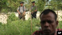 FILE - A Hindu man sits, seeking shelter, after fleeing violence that broke out on Aug. 25, as soldiers keep watch, in Maungdaw town, Rakhine state, Myanmar, Sept. 6, 2017.