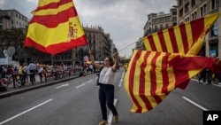 A woman waves flags of Catalonia and Spain as people celebrate a holiday known as "Dia de la Hispanidad" or Spain's National Day in Barcelona, Spain, Oct. 12, 2017. 