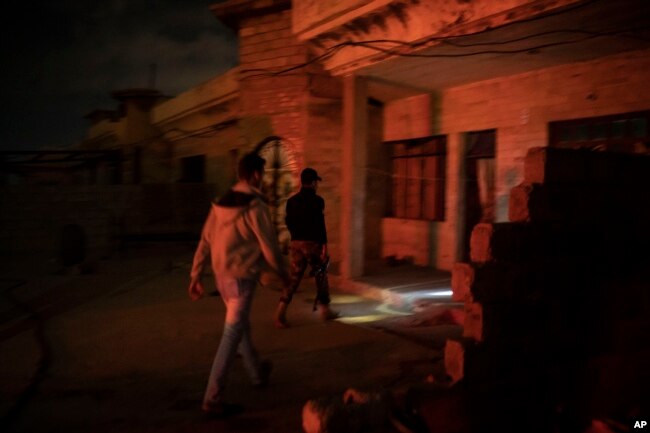 In this April 2, 2019 photo, an Iraqi army 20th division soldier walks with a civilian during a nighttime raid near Badoush, Iraq. The small town on the banks of the Tigris River was once one of the Islamic State group's most diehard strongholds.