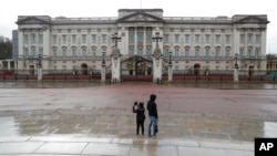 FILE - Two tourists stand in front of Buckingham Palace, one of the official homes of Britain's Queen Elizabeth II, in London, March 25, 2021. Britain is ending restrictive quarantine requirements for visitors from 47 countries, starting Oct. 11, 2021.