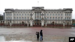 FILE - Two tourists stand in front of Buckingham Palace, one of the official homes of Britain's Queen Elizabeth II, in London, March 25, 2021. Britain is ending restrictive quarantine requirements for visitors from 47 countries, starting Oct. 11, 2021.