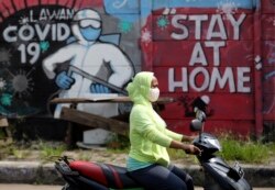 Seorang pengendara motor melintas di depan mural imbauan untuk tinggal di rumah di tengah pandemi virus corona, Jakarta, Juni 2020.