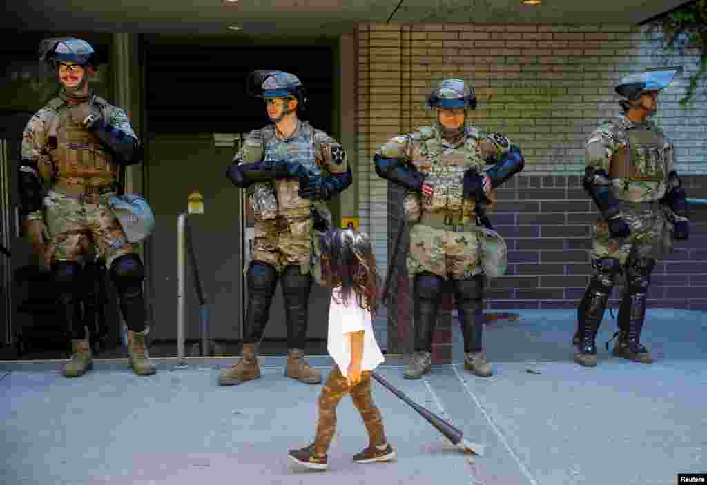 A child carrying a small broom walks past a line of National Guard members deployed to Bellevue Square as community members clean up after looting and damage that took place Sunday in Bellevue, Washington, June 1, 2020.