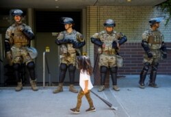 A child carrying a small broom walks by a line of National Guard members deployed to Bellevue Square as community members clean up after looting and vandalism that occurred Sunday at Bellevue Square in downtown Bellevue, Washington, U.S. June 1, 2020.