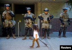 A child carrying a small broom walks by a line of National Guard members deployed to Bellevue Square as community members clean up after looting and vandalism that occurred Sunday at Bellevue Square in downtown Bellevue, Washington, U.S. June 1, 2020.