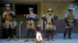 A child carrying a small broom walks by a line of National Guard members deployed to Bellevue Square as community members clean up after looting and vandalism that occurred Sunday at Bellevue Square in downtown Bellevue, Washington, U.S. June 1, 2020.