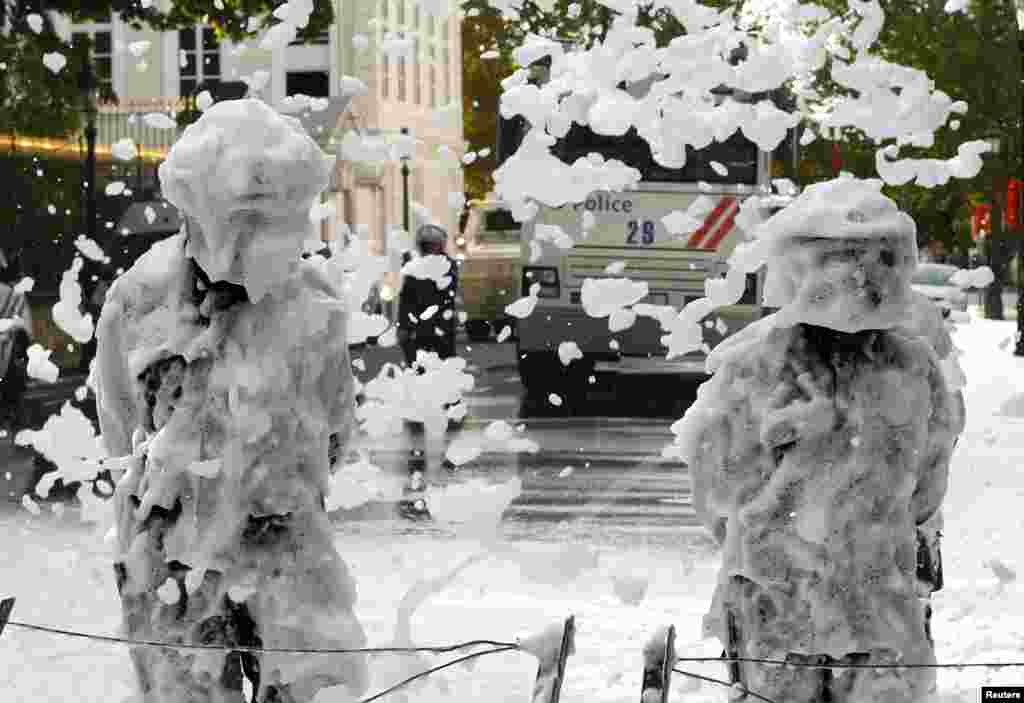 Belgian riot police stand as they are covered with foam sprayed by Belgian firefighters during a protest for better work conditions in central Brussels.