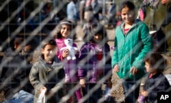 Anak-anak tersenyum ke kamera di belakang pagar di pusat penampungan sementara untuk migran di dekat garis perbatasan antara Serbia dan Hungaria di Roszke, Sabtu, 12 September 2015. (Foto: AP)