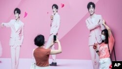 FILE - People take photos in front of a billboard with images of Anson Lo, a member of Cantopop boyband Mirror, in Hong Kong, Aug. 6, 2021.