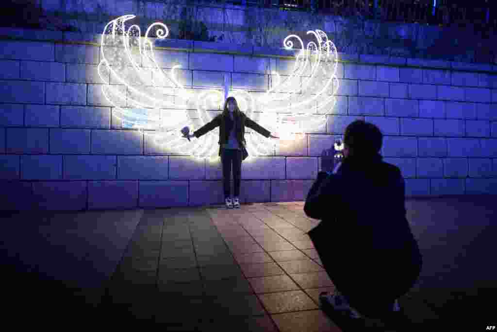 한국 서울 청계천에서 크리스마스 페스티벌이 열리는 가운데 한 여성이 천사 날개 모양의 조명 장식 앞에서 사진을 찍고 있다.