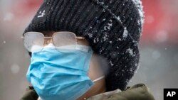 Una mujer en Beijing, usa una mascarilla al caminar por una calle de la ciudad durante una nevada, el domingo 2 de febrero de 2020. China informó que las muertes por el coronavirus de Wuhan subieron a 304.