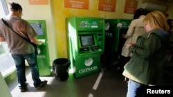 FILE - People use an ATM inside a branch of Sberbank in St. Petersburg, Russia, Sept. 16, 2014.