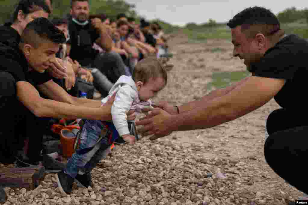 Eryko, a six-month-old asylum-seeking migrant from Romania, learns how to walk with the help of his brother Antonio, 16, and father Elvis, as they await with others to be transported to a U.S. border patrol processing facility after crossing the Rio Grand river into the United States from Mexico on a raft in La Joya, Texas, May 5, 2021.