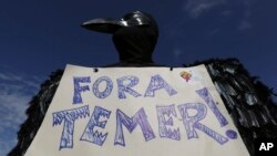FILE - A demonstrator dressed in a black feathered costume holds a sign telling Brazil's President Michel Temer to "get out," during an anti-government protest in Brasilia, May 24, 2017.